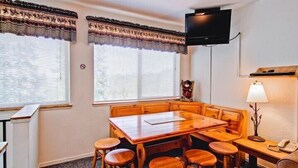 A room with a wooden table and benches, a television mounted on the wall, and a lamp on a side table. - Scenic Wonders Alpine View 2 Bedroom (Yosemite National Park)