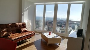 A spacious living room with a leather sofa, a coffee table, and a view of the city through large windows.