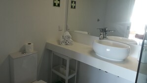 A modern bathroom with a white sink, a large mirror, and two small first aid signs on the wall.