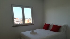 A bedroom with a bed, two red pillows, and a window with a city view.