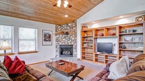A cozy living room with a stone fireplace, wooden shelves, and a television.