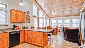 A spacious kitchen with wooden cabinets, a dishwasher, and a large island. There are multiple windows providing natural light, and a dining area with wooden chairs and a table. - Scenic Wonders  Bear Den 5 Bedrooms (Yosemite National Park)