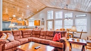 A spacious living room with a large brown sectional sofa, a wooden coffee table, and a dining area with a table and chairs. - Scenic Wonders  Bear Den 5 Bedrooms (Yosemite National Park)