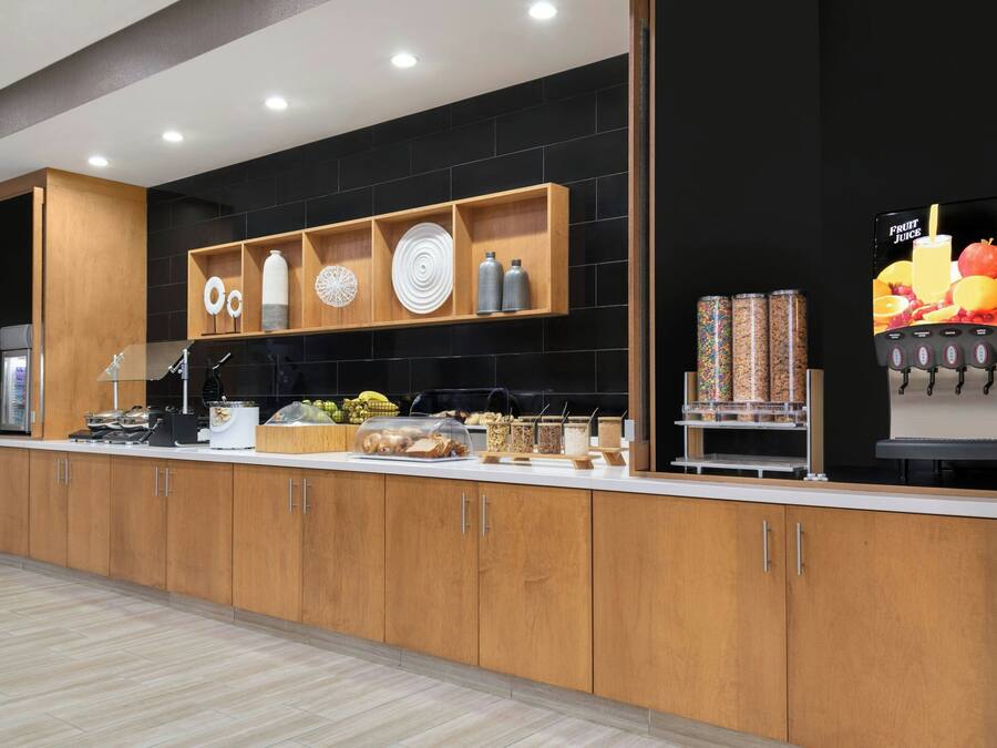 Una cocina moderna con armarios de madera, un dispensador de jugo de frutas incorporado y diversos alimentos sobre la encimera.