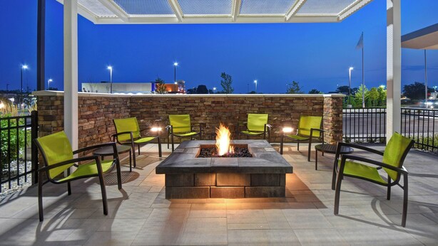 A fire pit surrounded by chairs in an outdoor patio area with a stone wall and a view of the cityscape at dusk. - SpringHill Suites by Marriott Holland (Holland)