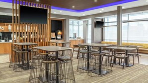 A modern restaurant with multiple tables and bar stools, a wooden partition with vertical slats, and a large flat-screen TV mounted on the wall. - SpringHill Suites by Marriott Holland (Holland)