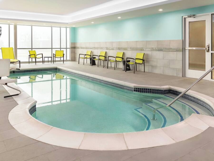 An indoor swimming pool with a tiled edge, yellow chairs, and a glass door.