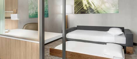 A modern hotel room with a bunk bed, a desk with a chair, a lamp, and two abstract paintings on the wall.