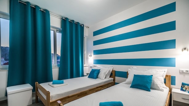 A room with two beds, a window with curtains, and a wall with blue stripes. - Apartments Sunshine Home - Twin Room (Blue) (Vela Luka)