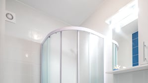 A modern bathroom with a glass shower enclosure, a white toilet with a blue lid, and a white sink with a mirror above it. - Apartments Sunshine Home - Twin Room (Blue) (Vela Luka)