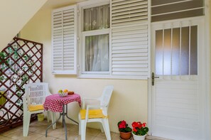 A patio with two white plastic chairs, a small table with a checkered tablecloth, and a potted plant with red flowers. - Apartment Petrana - Studio Apartment with Terrace (Dubrovnik)