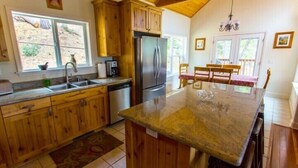 A kitchen with wooden cabinets, a stainless steel refrigerator, a dishwasher, and a large island with a glass top. - Scenic Wonders Birds Eye Vista 3 Bedroom (Yosemite National Park)
