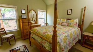 A bedroom with a four-poster bed, a wooden dresser, a chair, and a mirror.