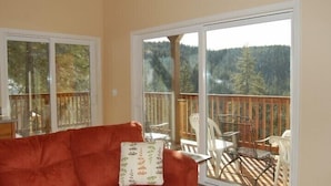 A room with a red sofa, a small table, and a chair. There is a large sliding glass door leading to a balcony with a wooden deck and chairs. - Scenic Wonders Birds Eye Vista 3 Bedroom (Yosemite National Park)