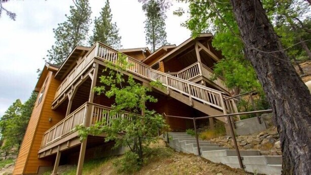 A wooden cabin with a staircase leading to a balcony, surrounded by trees. - Scenic Wonders Birds Eye Vista 3 Bedroom (Yosemite National Park)