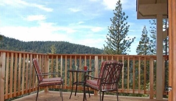 A wooden deck with two chairs and a small table, overlooking a forested hillside.