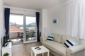 A living room with a sofa, a coffee table, and a sliding glass door leading to a balcony with a table and chairs.