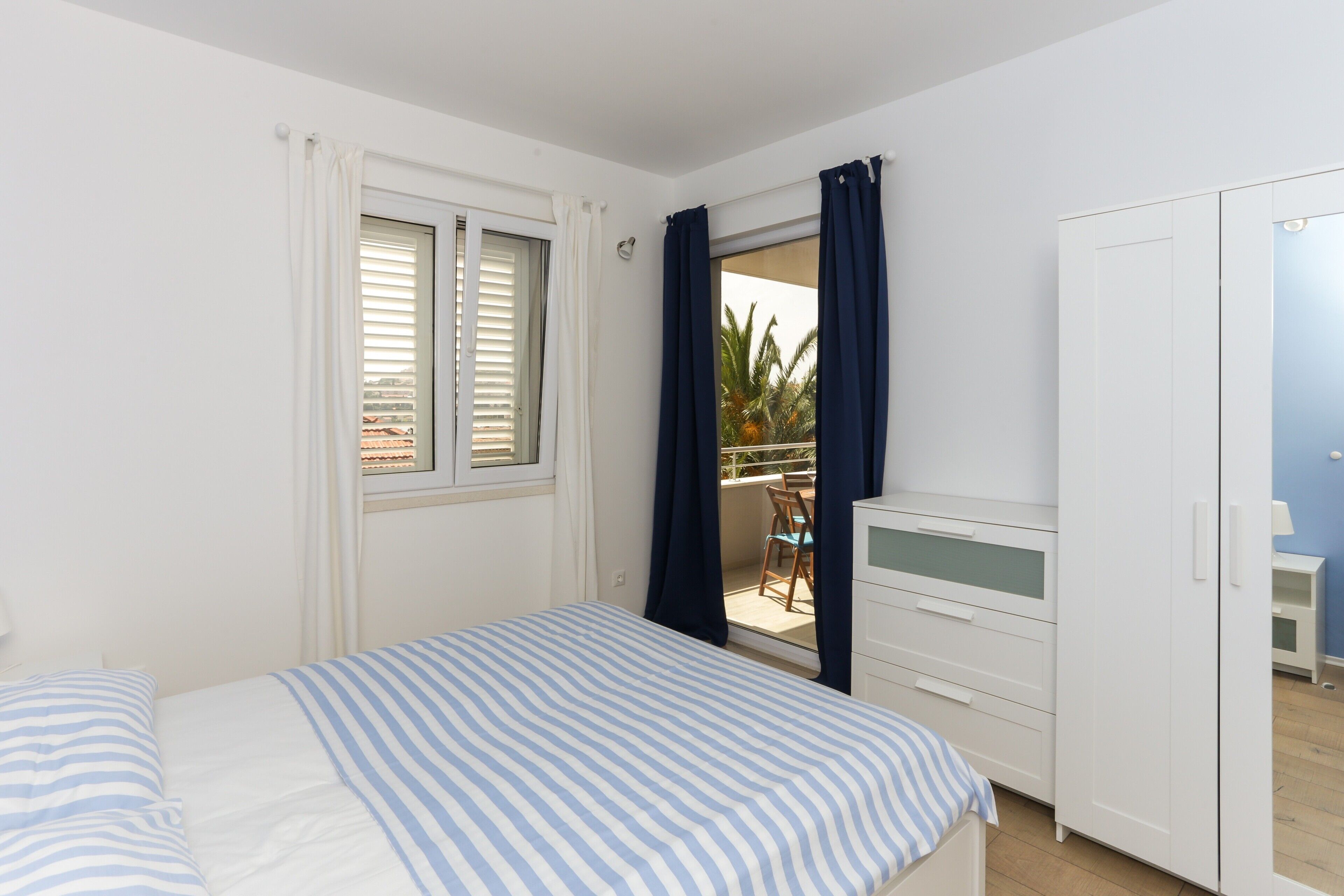 A bedroom with a bed, a wardrobe, and a balcony with a chair and table.
