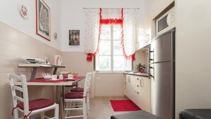 Cocina compacta con comedor, que incluye un refrigerador, una mesita con sillas y un ventanal con cortinas.