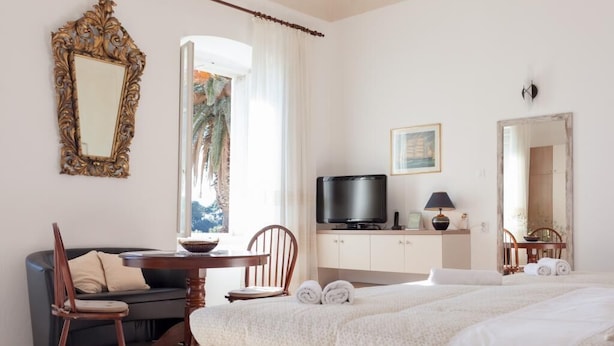 Una habitación de hotel con cama, televisor, mesa de comedor con sillas, sofá y un espejo grande.
