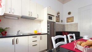 Una cocina moderna con armarios blancos, un refrigerador de acero inoxidable y un microondas. Hay una mesa de comedor con sillas y un mantel individual rojo.