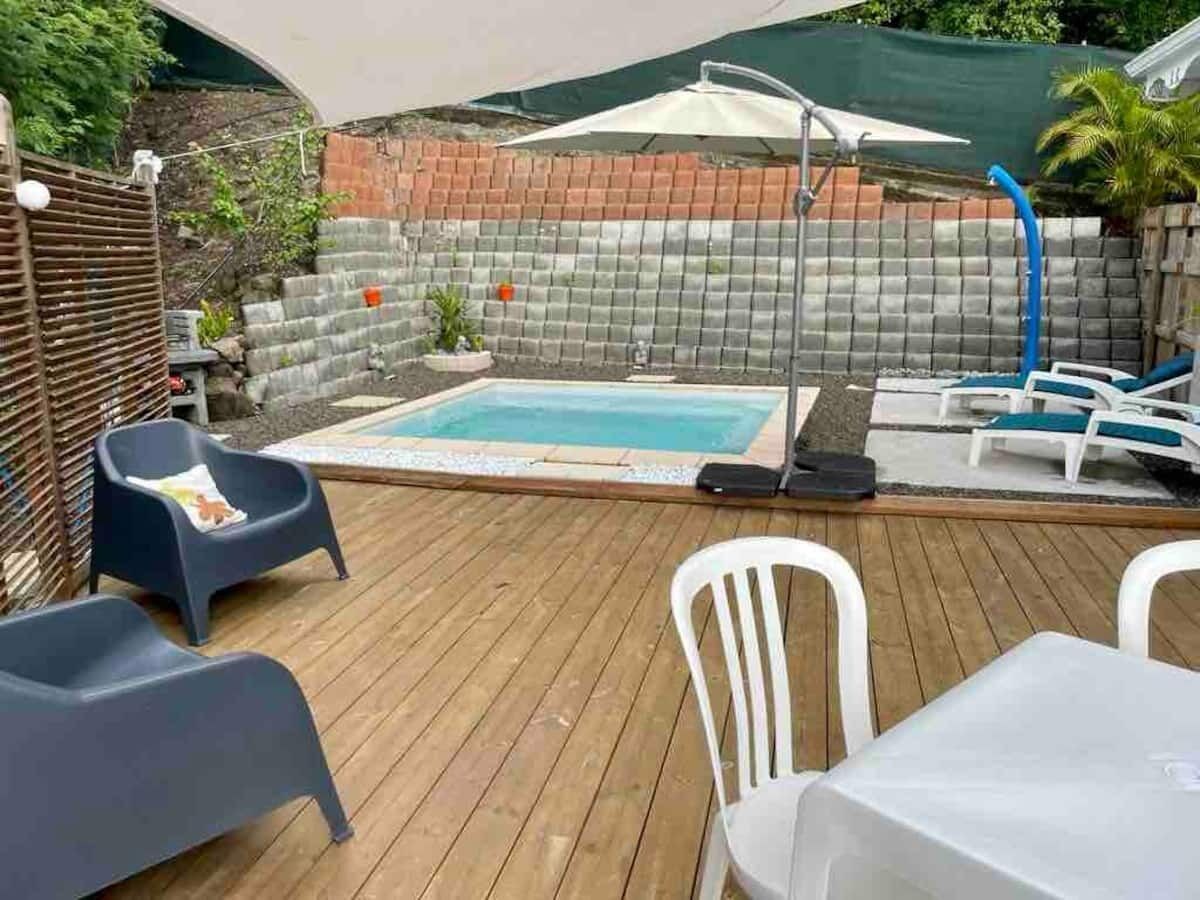 Una terraza de madera con una piscina pequeña, sillas de descanso y una mesa.