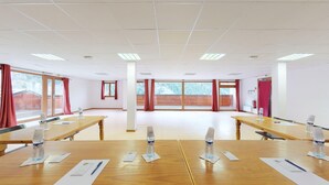A conference room with wooden tables, chairs, and large windows with red curtains. - Hameau 4 206 - SPA & PISCINE appartement 4 pers (Orelle)