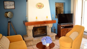 A living room with a fireplace, a sofa, a chair, and a television. - Charming house in a quiet (Guengat)