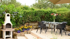 A patio with a stone fireplace, outdoor seating, and a variety of flowers. - Charming house in a quiet (Guengat)