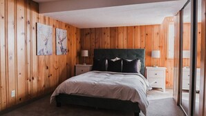 Ein Schlafzimmer mit einer holzgetäfelten Wand, einem Bett mit dunklem Kopfteil, zwei Nachttischen mit Lampen und zwei Wandbildern.