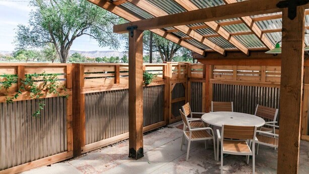 Ein überdachter Patio-Bereich mit einer Holz-Pergola, einem runden Tisch mit Stühlen und Blick auf Bäume und Berge im Hintergrund.