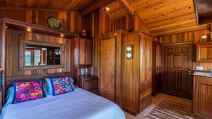 Interior d'una cabana de fusta amb un llit, un rellotge i un armari.