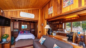 Interior acollidor d'una cabana amb decoració de fusta, un llit, un sofà, una cuina i una taula de menjador.