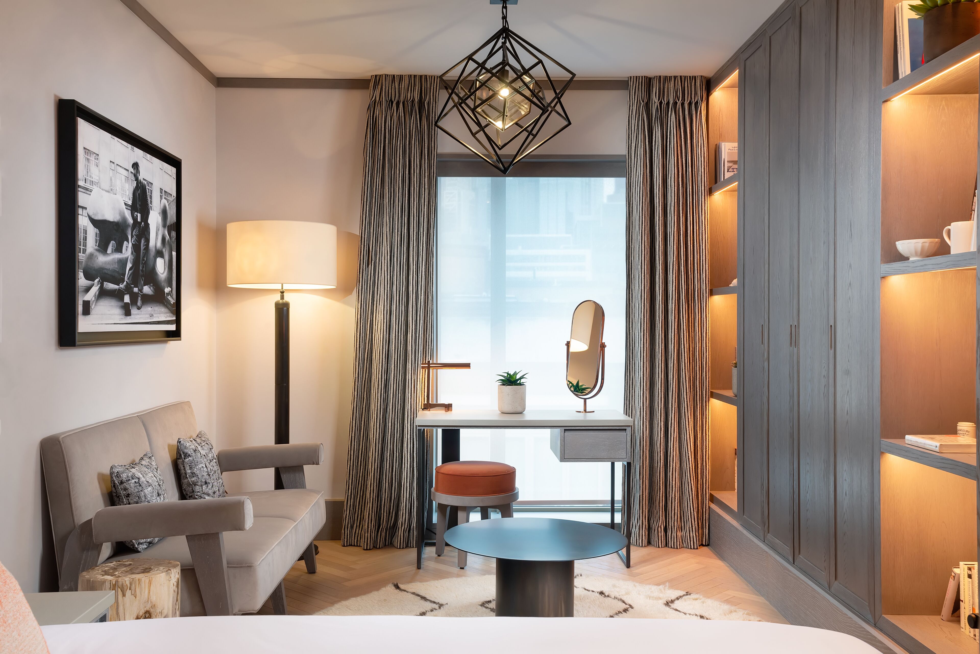 Ein modernes Zimmer mit Sofa, Schreibtisch, rundem Tisch und einem großen Fenster mit Vorhängen.
