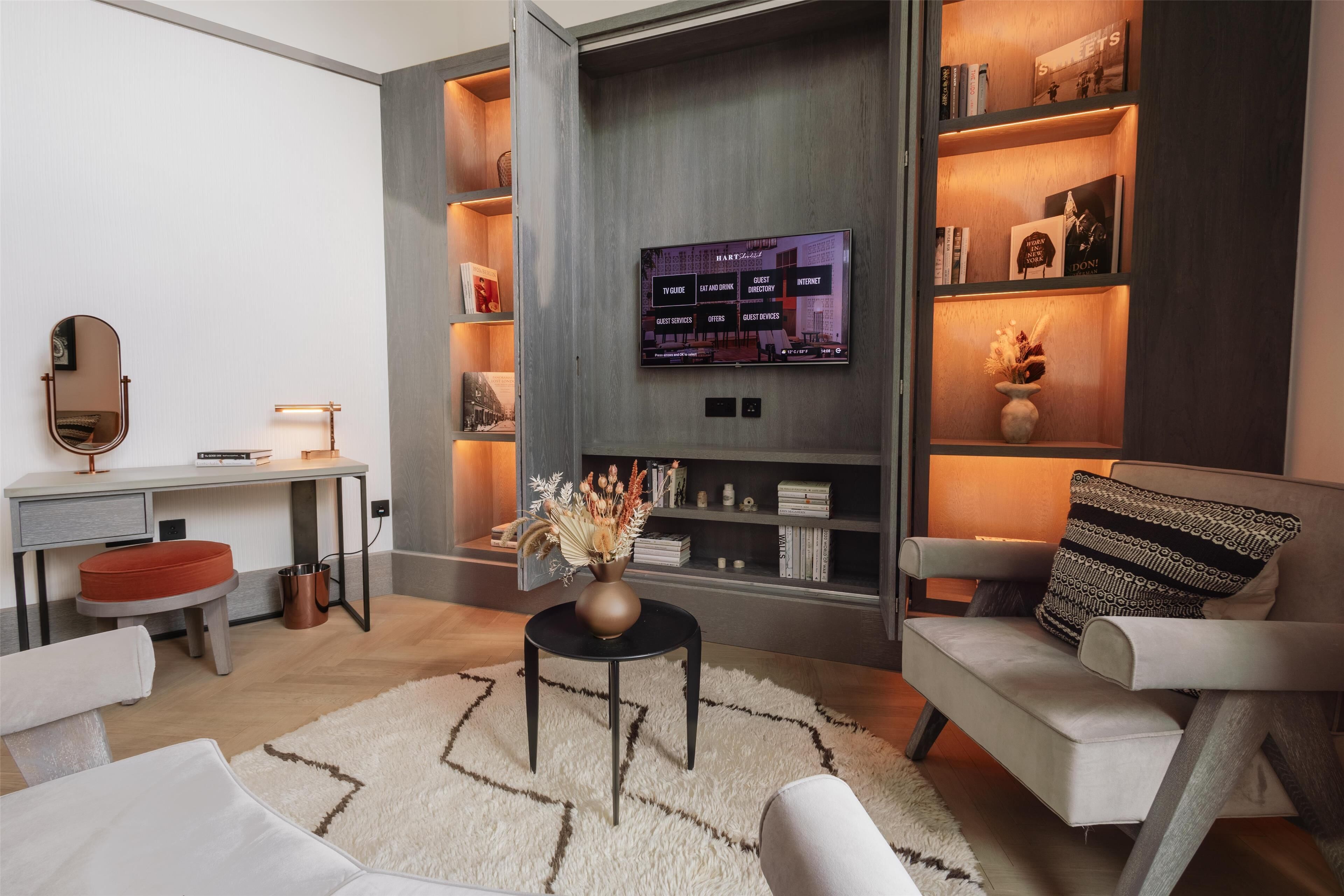 A modern living room with a flat-screen TV mounted on a wall, a round table with a vase, and a sofa with patterned cushions.