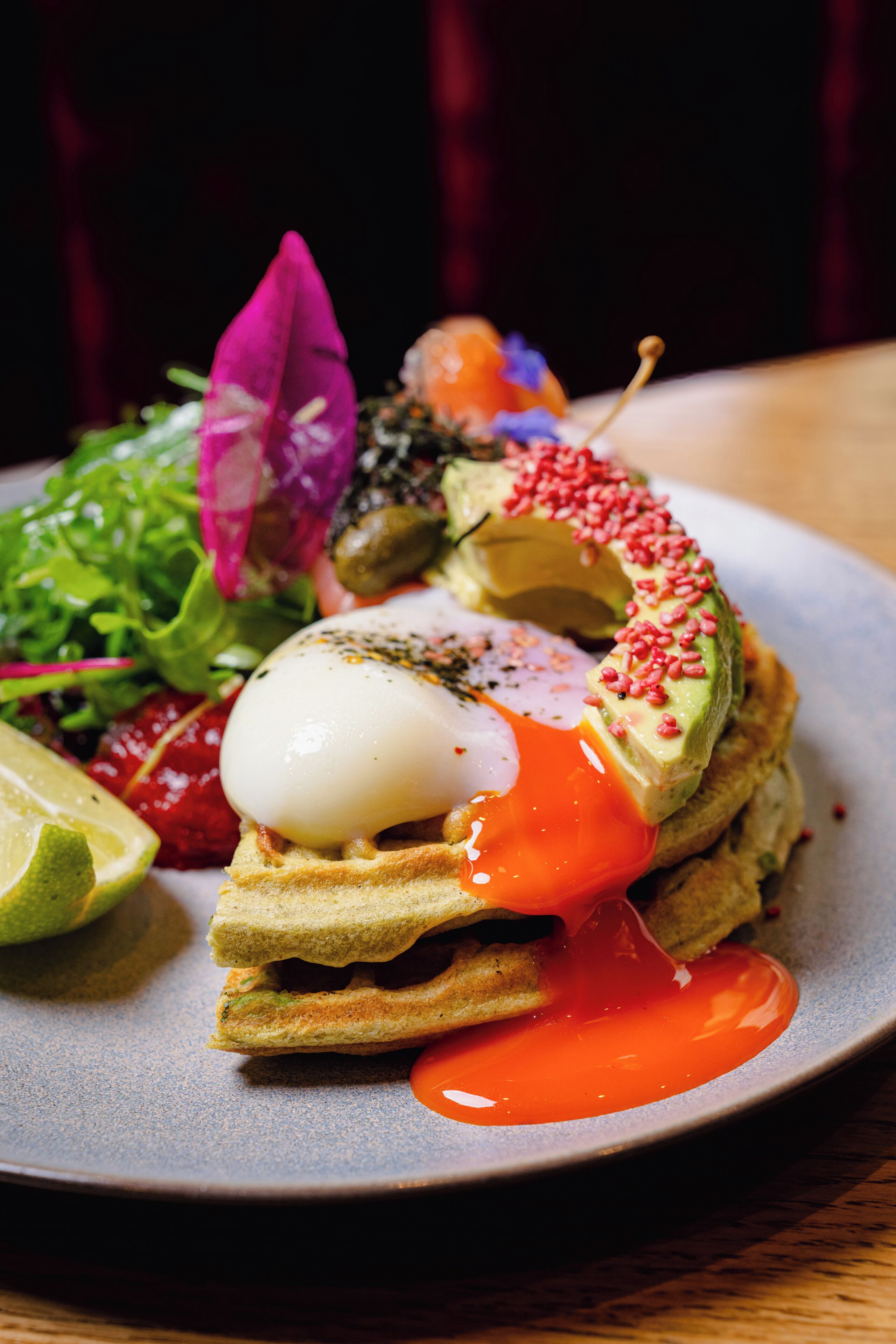 A plate of food with a poached egg, avocado, and sauce.