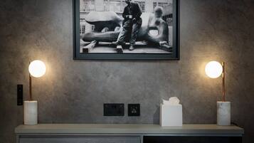 A modern room with a large framed photograph on the wall, two wall-mounted lamps, a white tissue box, and a built-in bookshelf with books.