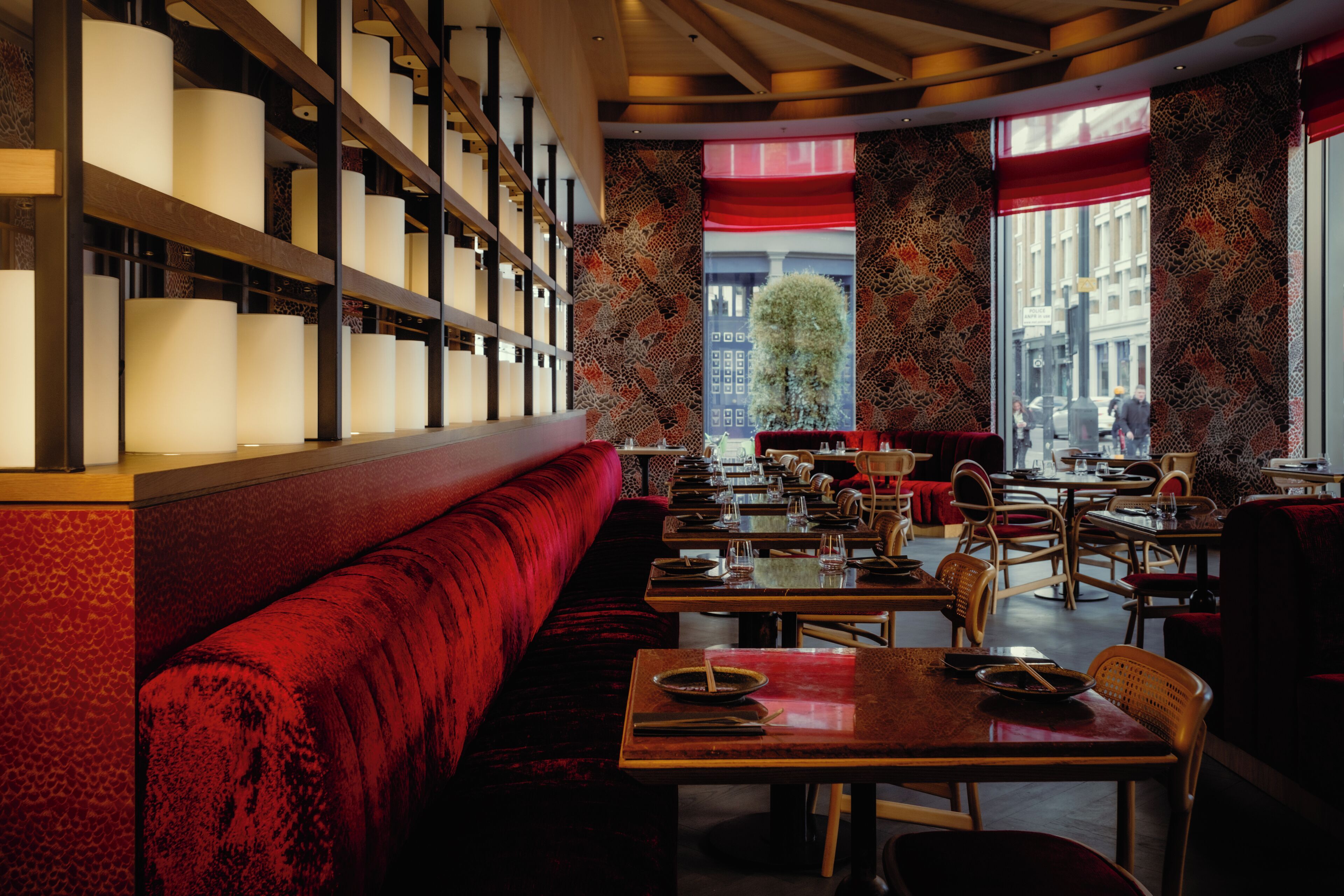 A restaurant with a red upholstered bench, wooden tables, and chairs.