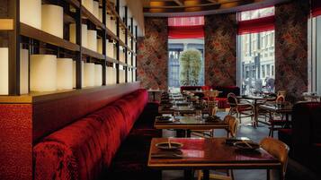 Un restaurante con un banco tapizado en rojo, mesas y sillas de madera.