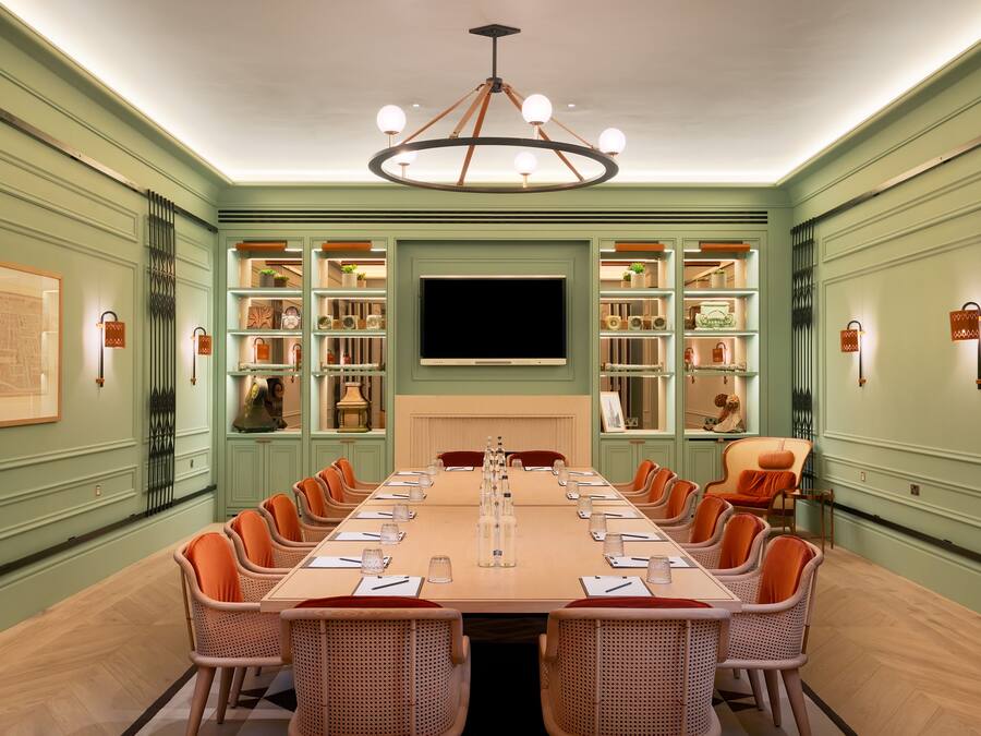 A conference room with a long table, chairs, a chandelier, and shelves with decorative items.