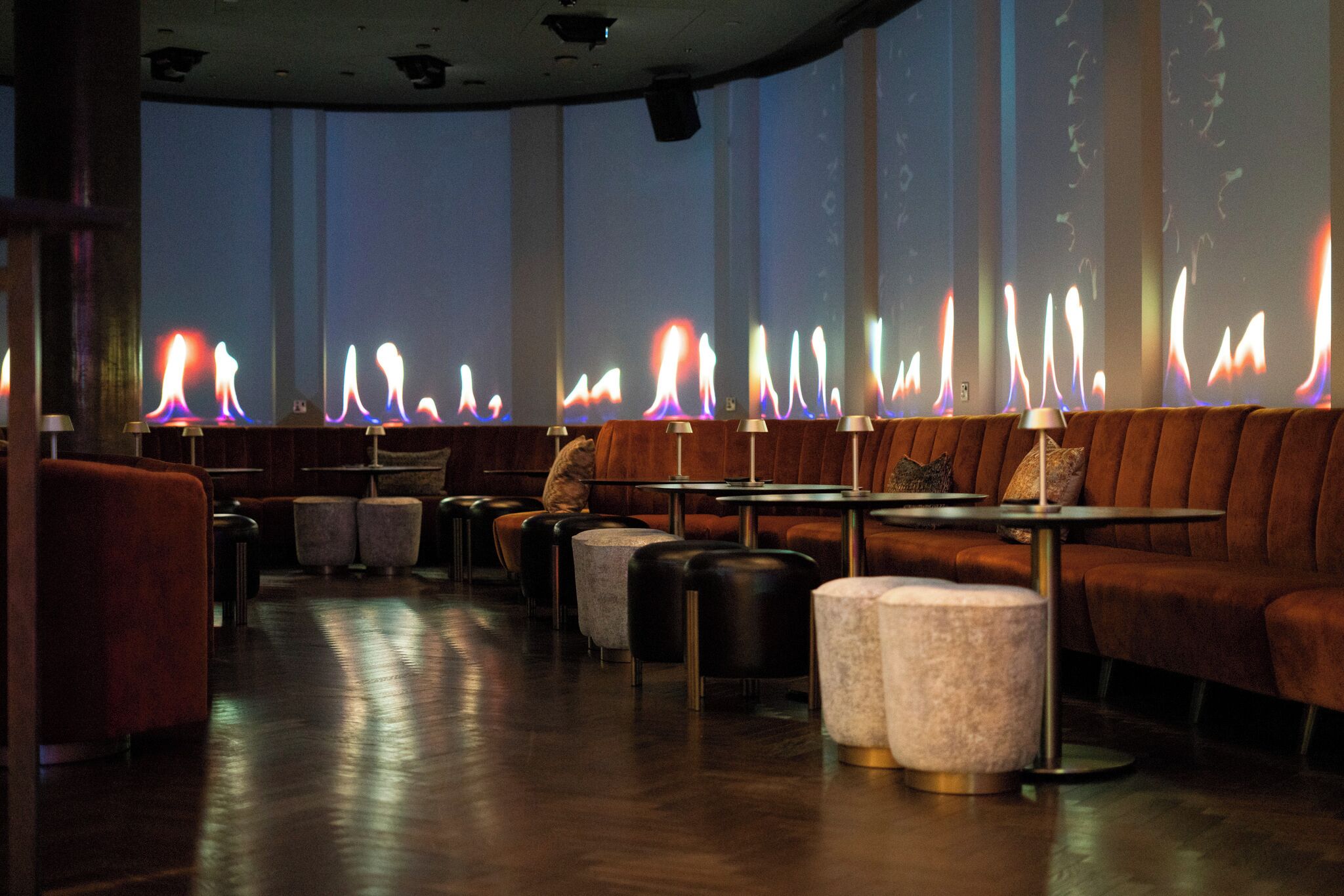 A restaurant with a long counter, cushioned seating, and a fireplace with colorful flames.