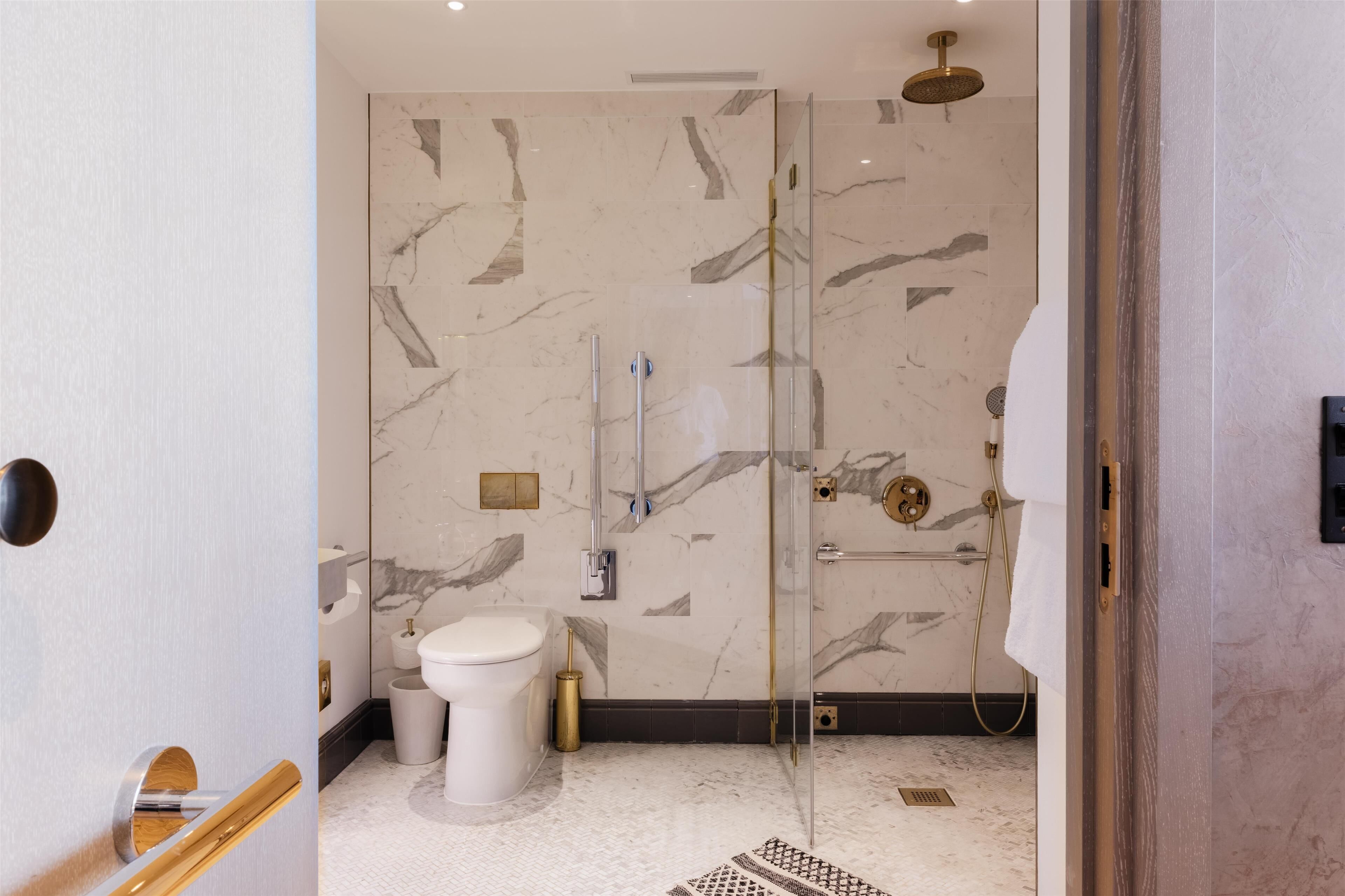 Une salle de bain moderne avec une douche à parois de verre, des murs en marbre et des toilettes blanches.