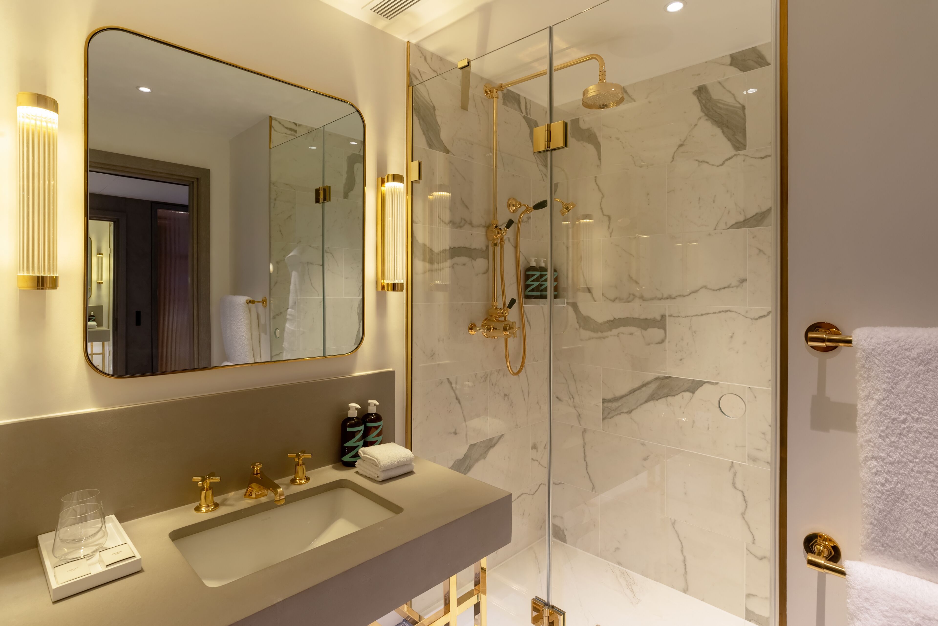 A modern bathroom with a large mirror, a sink with gold fixtures, and a glass-enclosed shower area.