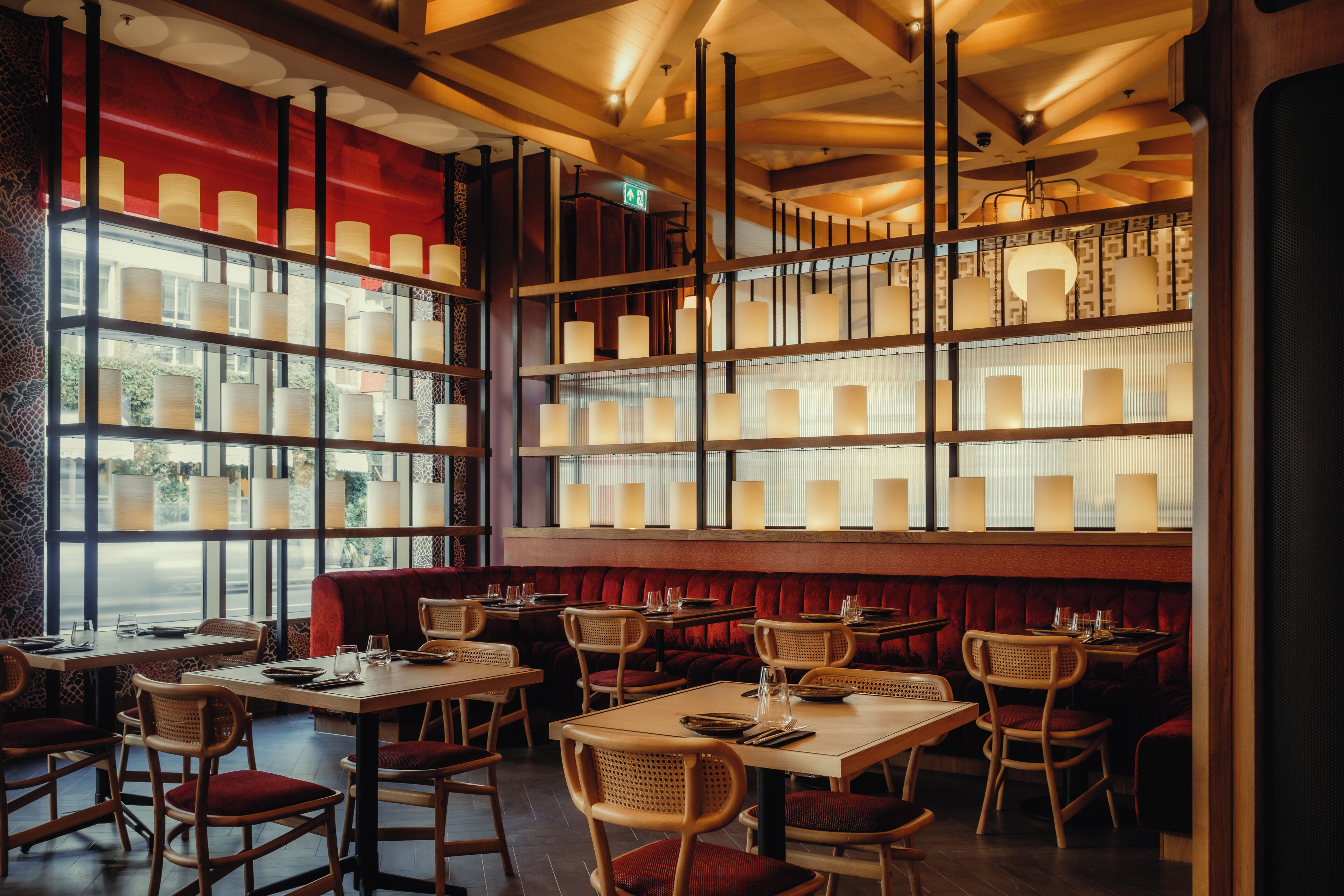 A restaurant interior with multiple tables and booths, wooden chairs, and a red cushioned bench area.