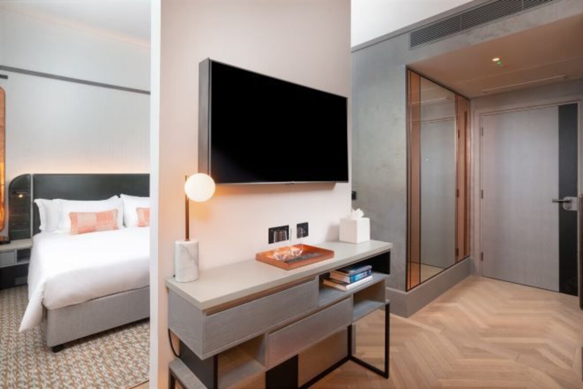Ett modernt hotellrum med en säng, ett skrivbord med en platt-TV, ett sängbord med en lampa och en stor spegel.