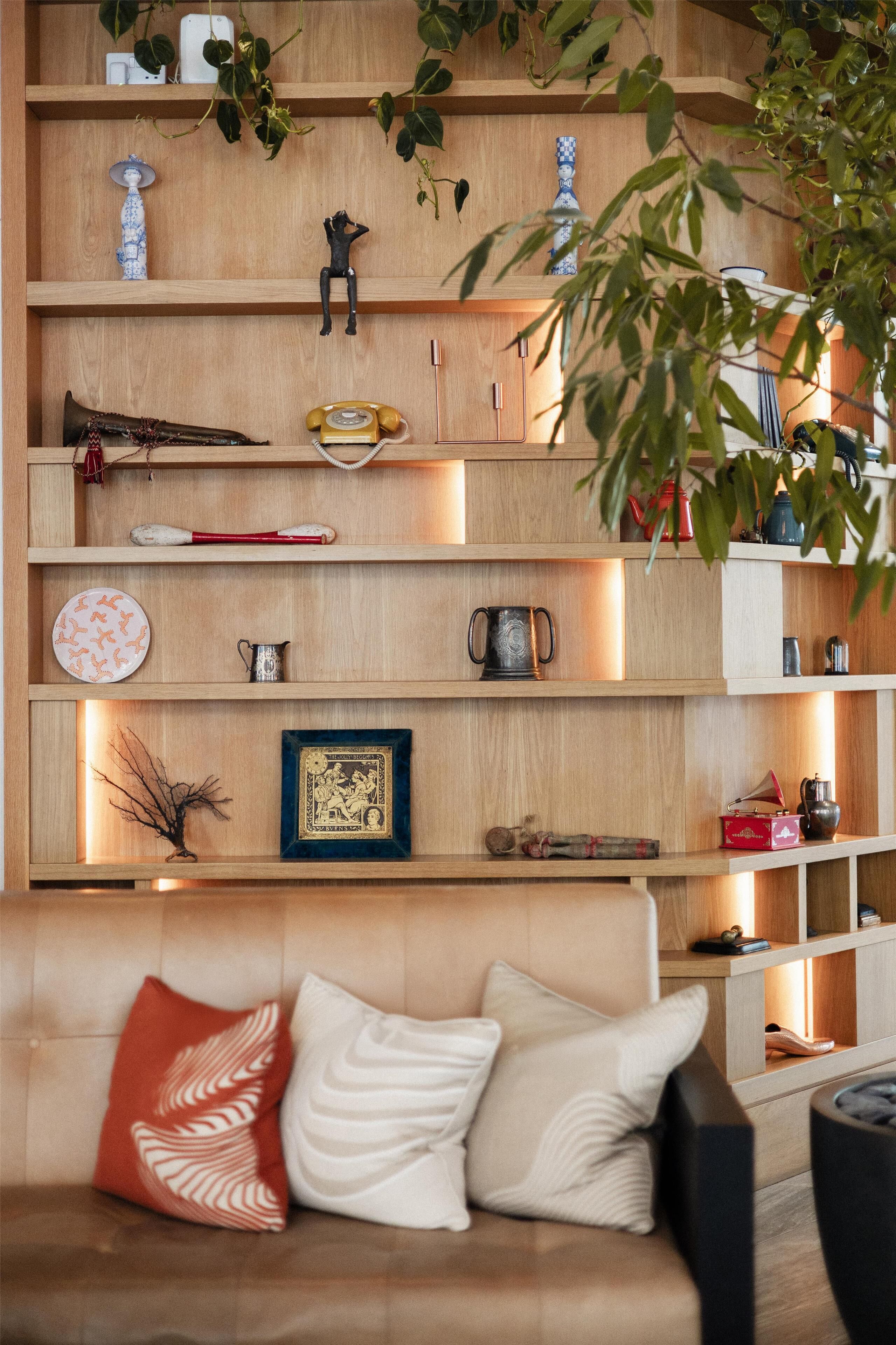 A wooden shelving unit with various decorative items and a sofa with cushions.
