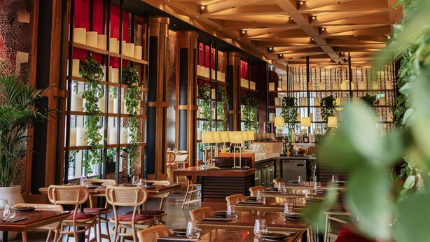 Un restaurant amb bigues de fusta al sostre, taules amb caires i seients tapissats de color vermell.
