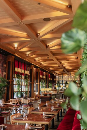 A restaurant with wooden ceiling beams, tables with chairs, and red upholstered seating.