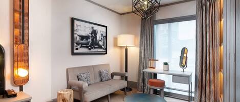 A modern living room with a sofa, a round coffee table, a lamp, a framed picture on the wall, and a window with curtains.