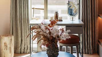 A modern room with a geometric pendant light, a round table with a vase of dried flowers, a mirror, and striped curtains.